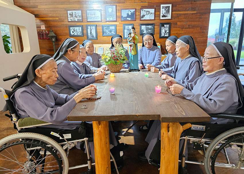 Older Sisters of Mary Sisters seated around a table, praying together in community.