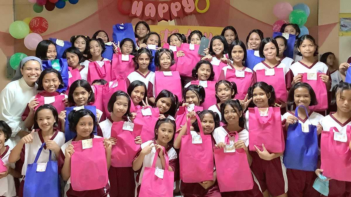 Students at Biga Girlstown smile with a Sister while holding colorful gift bags during an Every Child’s Birthday celebration.