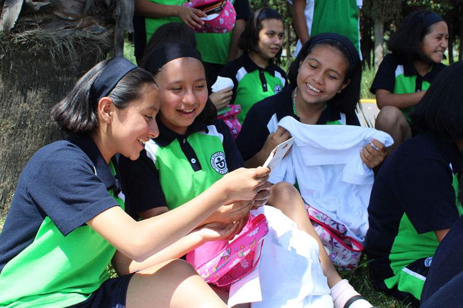 Students at Chalco Girlstown smile as one girl reads a birthday card and another holds up a white T-shirt during an outdoor celebration.
