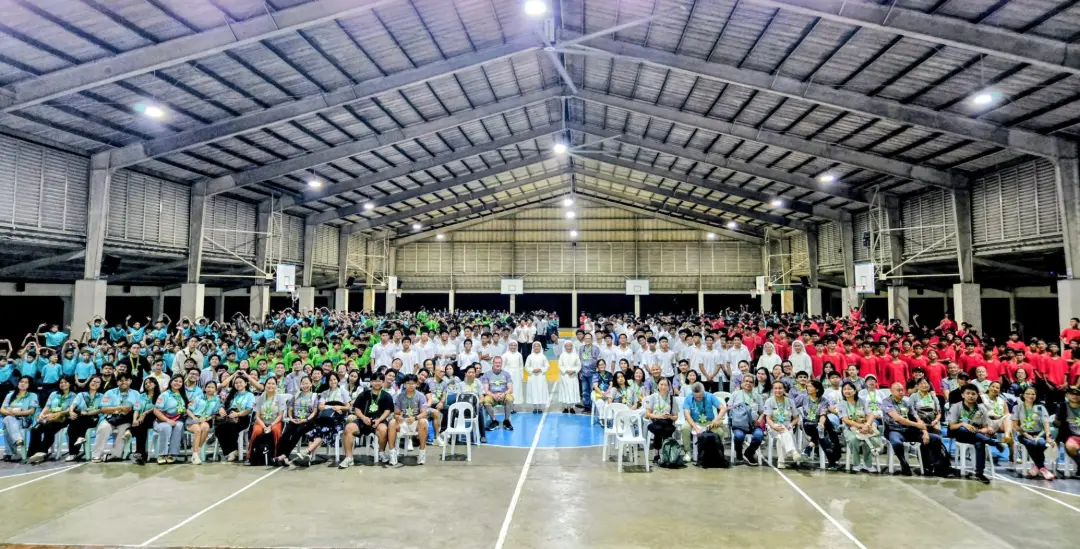 Anthony Sollano joins Sisters, graduates, and students for a large group photo inside a school gymnasium.